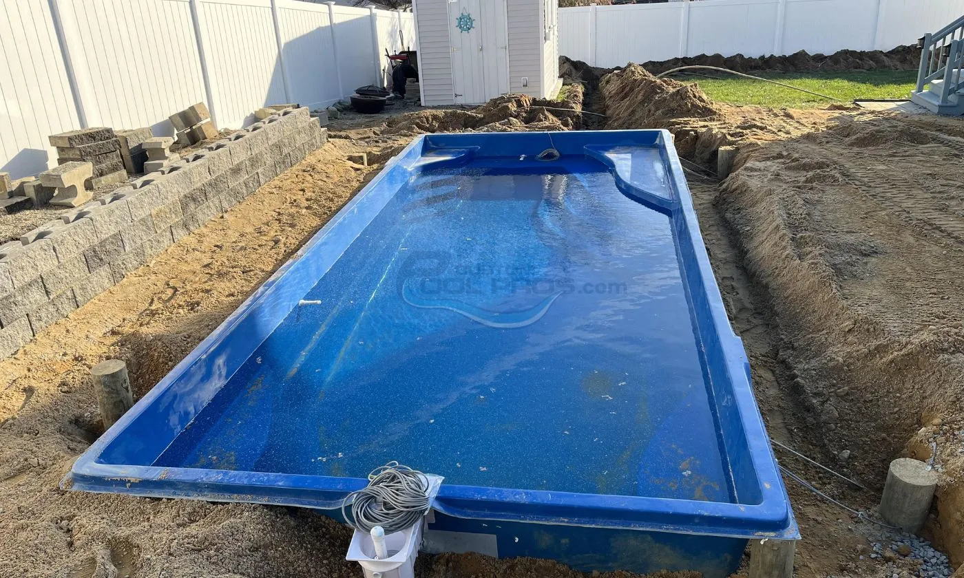 In-ground swimming pool installation in progress, featuring a blue fiberglass pool shell surrounded by excavated soil and construction materials.