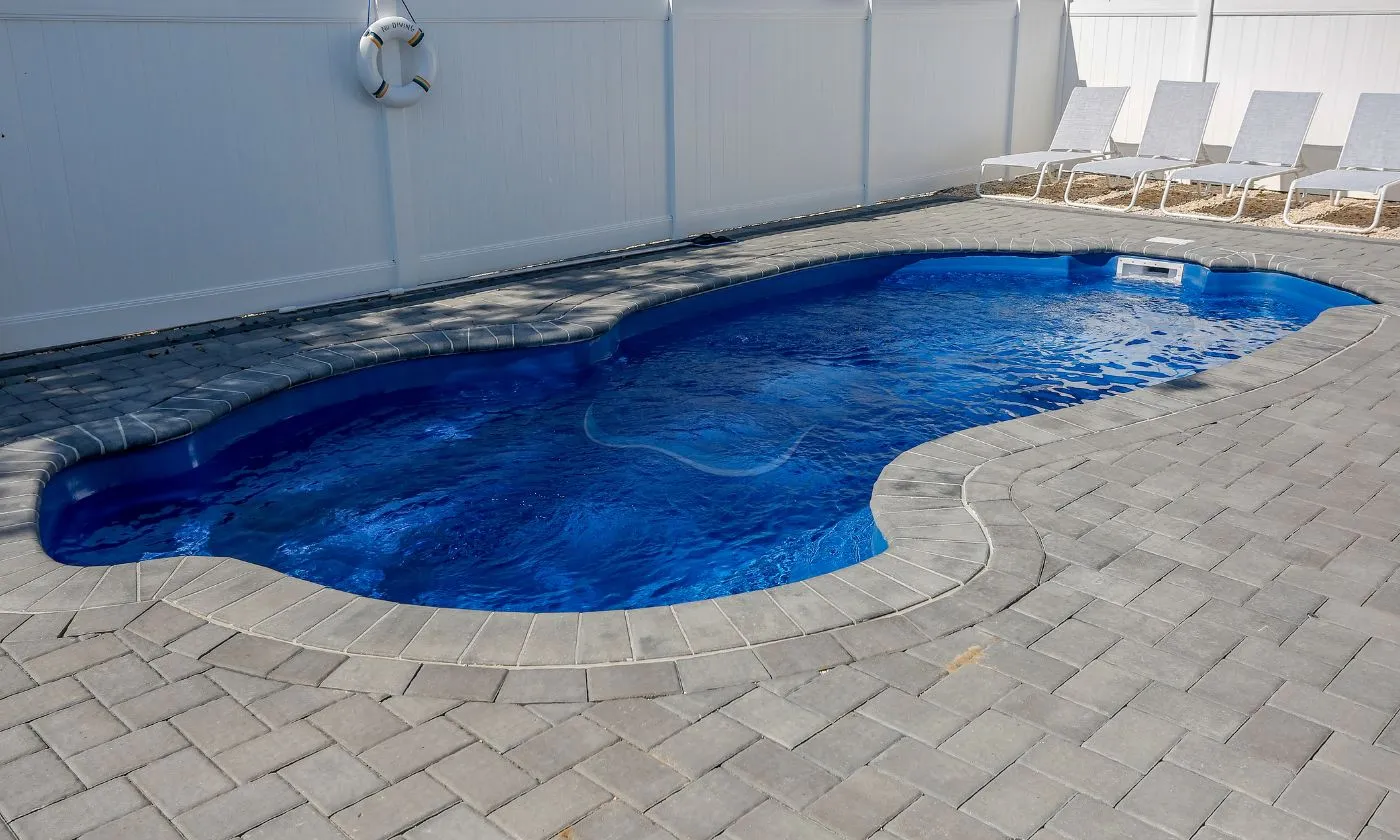 In-ground swimming pool with a vibrant blue interior and a stone patio, surrounded by a white fence, ideal for outdoor relaxation and recreation.