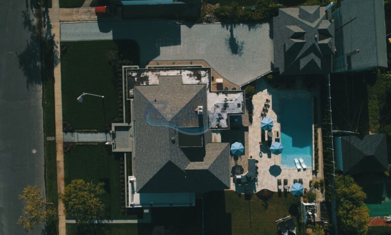 Aerial view of a modern residential property featuring a large swimming pool, sun loungers, and patio umbrellas, surrounded by landscaped gardens and driveways, pool contractors nj, backyard pool