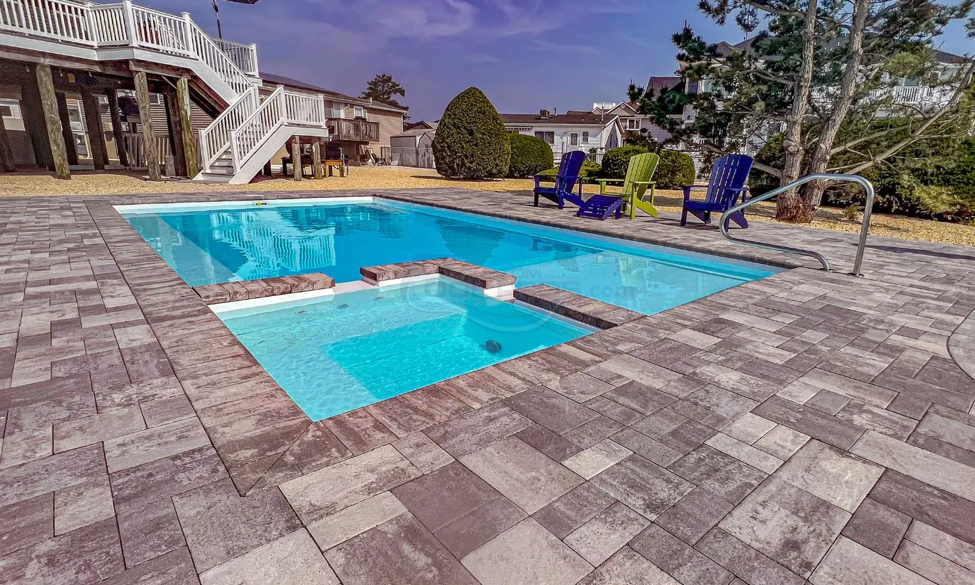 Modern backyard swimming pool with a clear blue water, surrounded by paver stones and colorful lounge chairs, ideal for relaxation and outdoor gatherings.