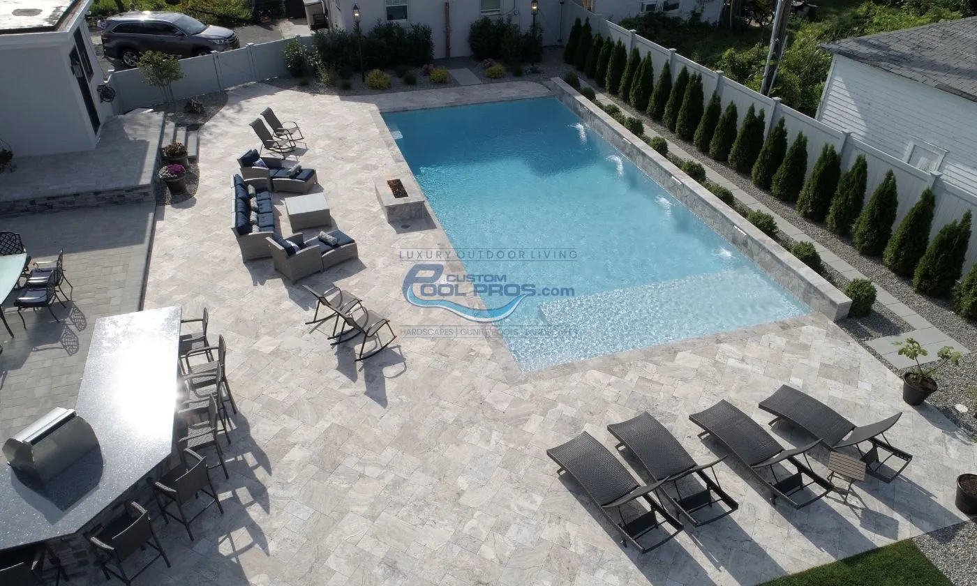 rectangular style inground pool with sun tanning ledge, pool deck with lounge chairs, outdoor sitting area, firepit by luxury pool