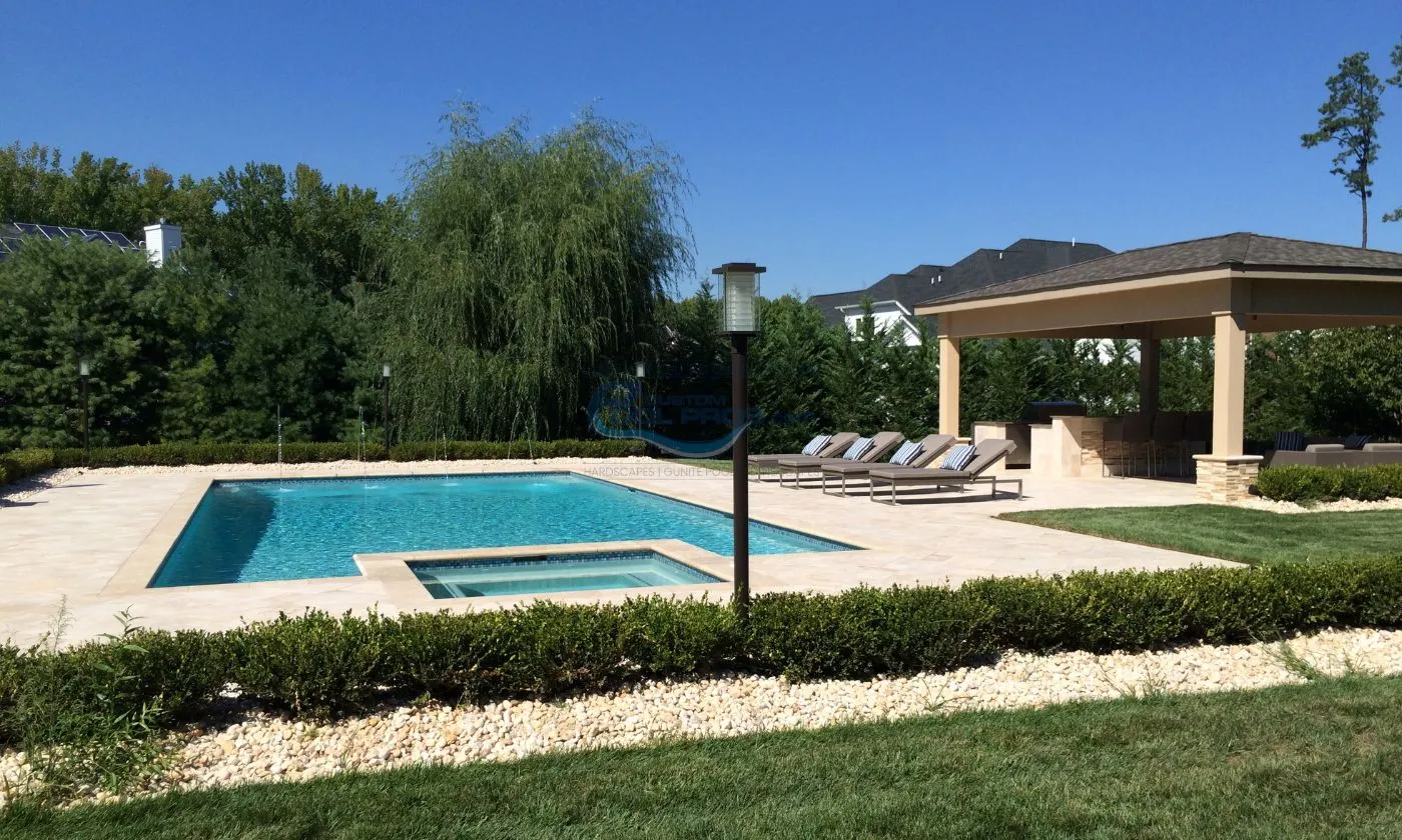 rectangular inground pool with square spa, lamp, pool patio with lounge chairs by pool pavilion, pool builder, inground pool